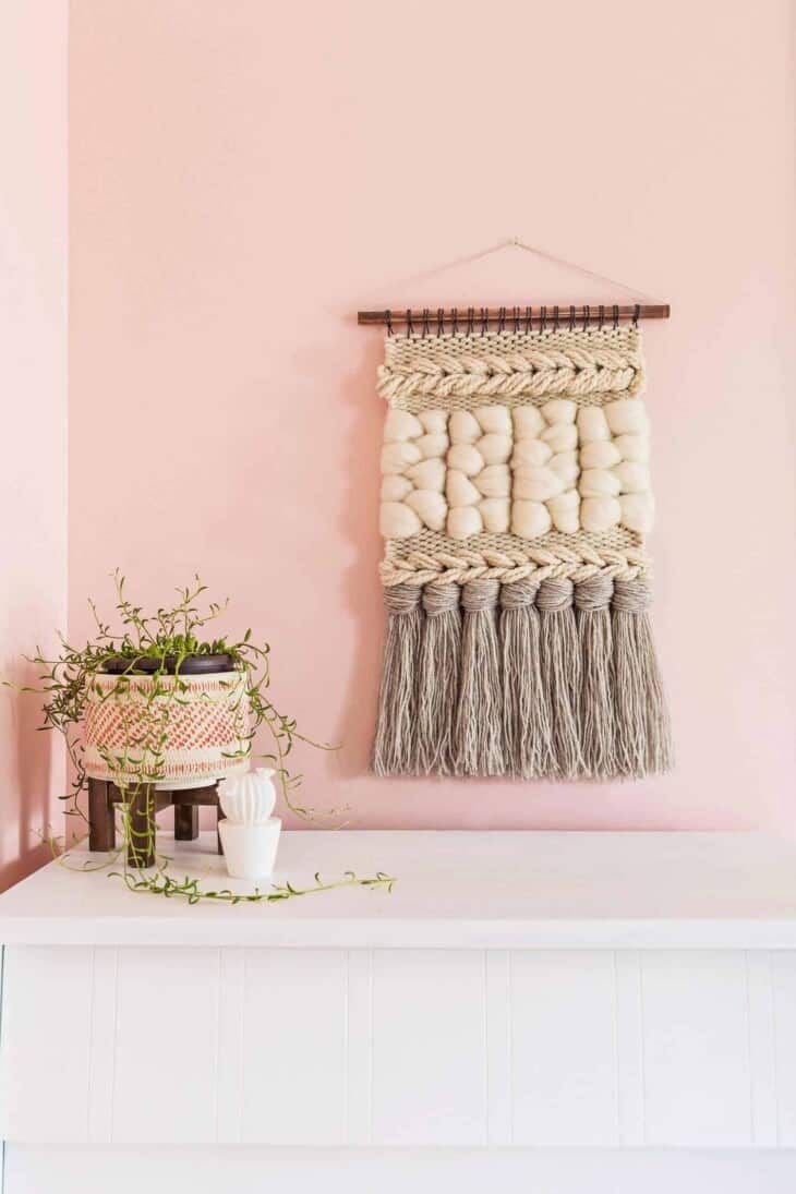 A yarn wall hanging on a pink wall