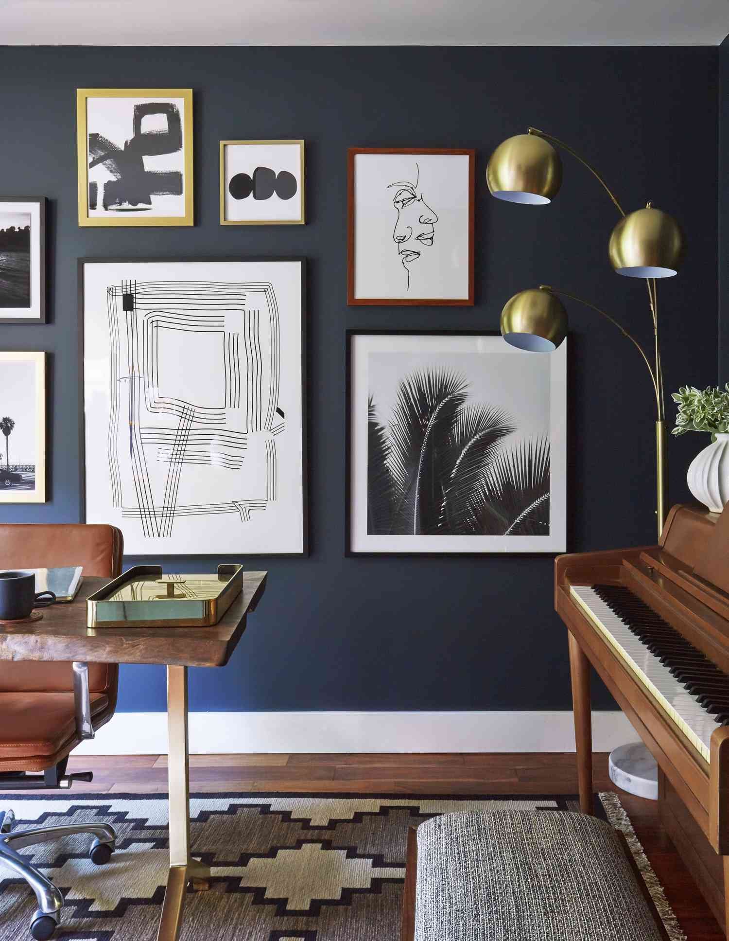 Brass three-arm floor lamp in a home office with dark paint color and eclectic gallery wall