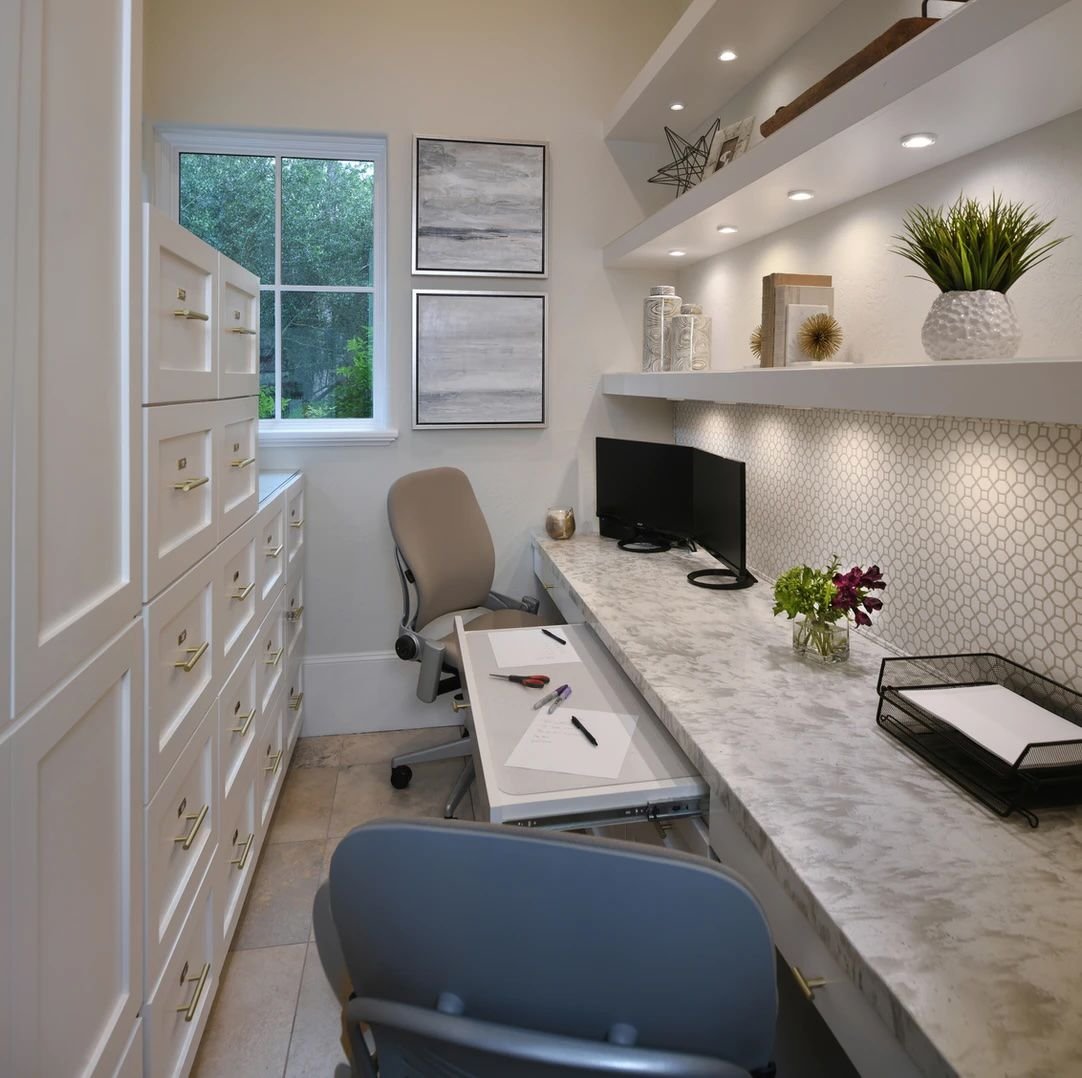 Lights under floating shelves above a built-in desk in a white home office
