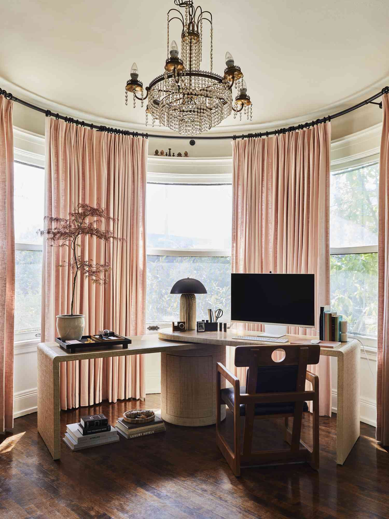 Chrystal chandelier hanging in a home office with bay window and pink curtain panels